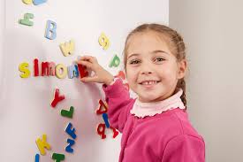 Little girl with a big smile and playing with abc magnet letters on a white fridge front
